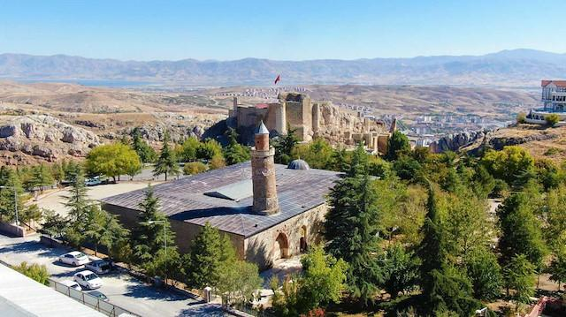 Tourists visiting a historic landmark in Elazığ with surrounding buildings.