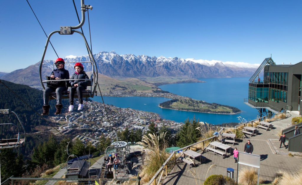 Tourists enjoying activities along Lake Wakatipu in Queenstown with mountains in the background.